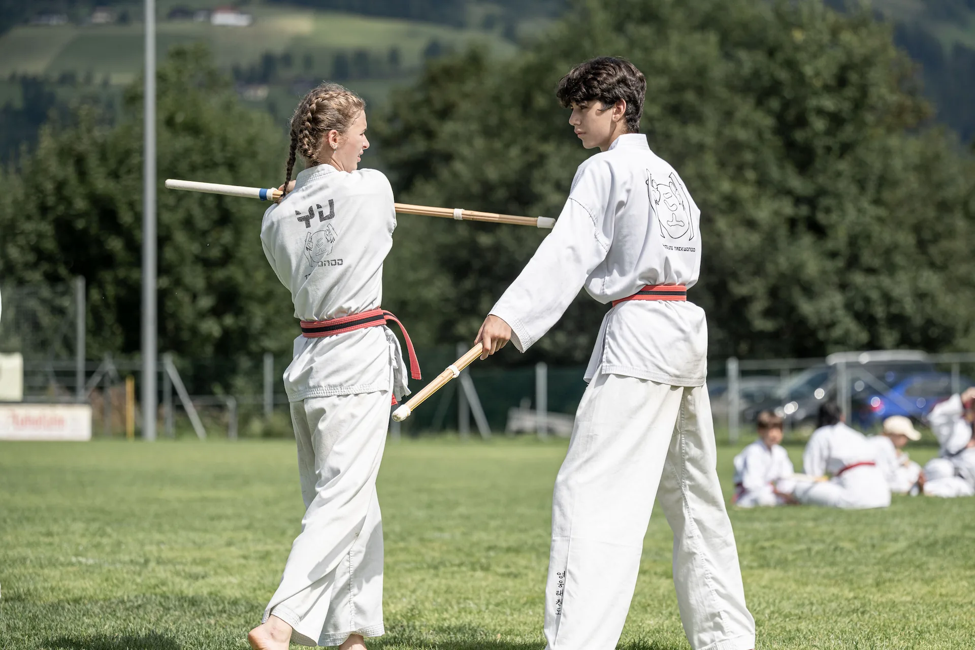 Zwei Jugendliche in Taekwondo-Uniformen üben bei einem Shinai-Workshop Techniken mit Bambusschwertern im Freien.