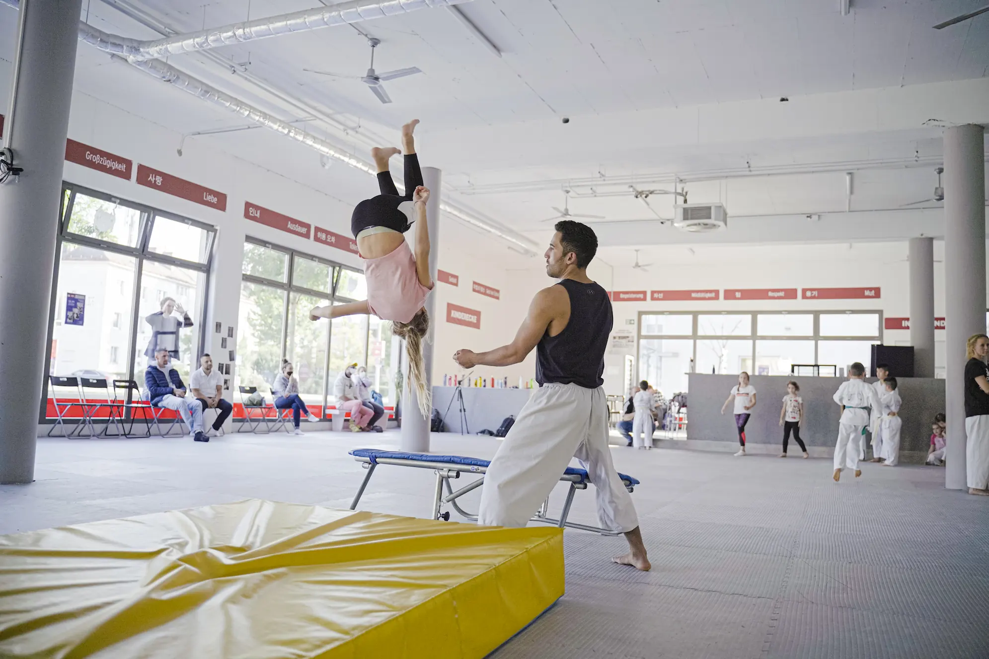 Junges Mädchen übt einen Salto im Taekwondo-Akrobatik-Training unter Anleitung eines Trainers im Dojang.