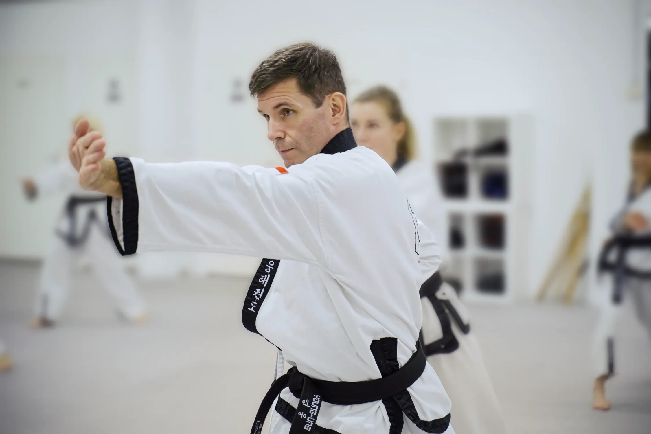 Taekwondo-Schwarzgurt führt konzentriert eine Hyong-Technik beim Formenlauf im Trainingsraum aus.