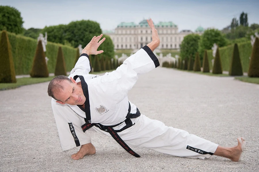 Taekwondo-Sportler im Kimoodo-Anzug führt eine tiefe Dehnübung vor dem Schloss Belvedere in Wien aus.