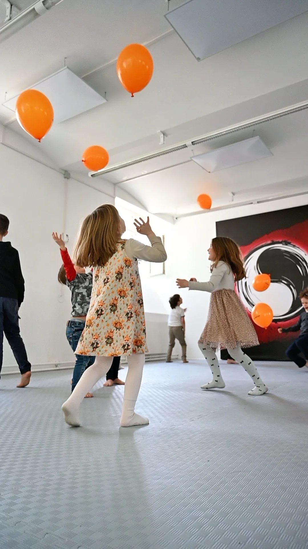 Spielerisches Taekwondo-Kindertraining: Kinder balancieren orangefarbene Luftballons im Trainingsraum zur Förderung der Koordination.