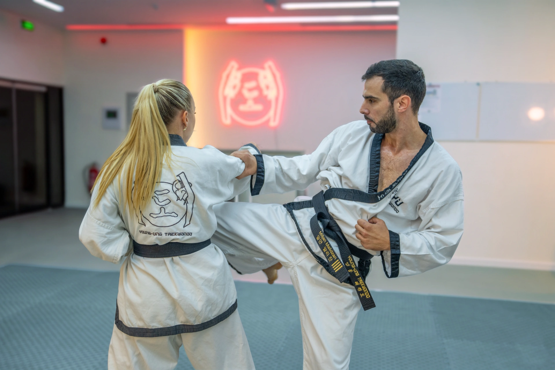 Taekwondo Privatstunden für Erwachsene: Ein Mann mit Schwarzgurt übt einen hohen Tritt mit einer Partnerin.