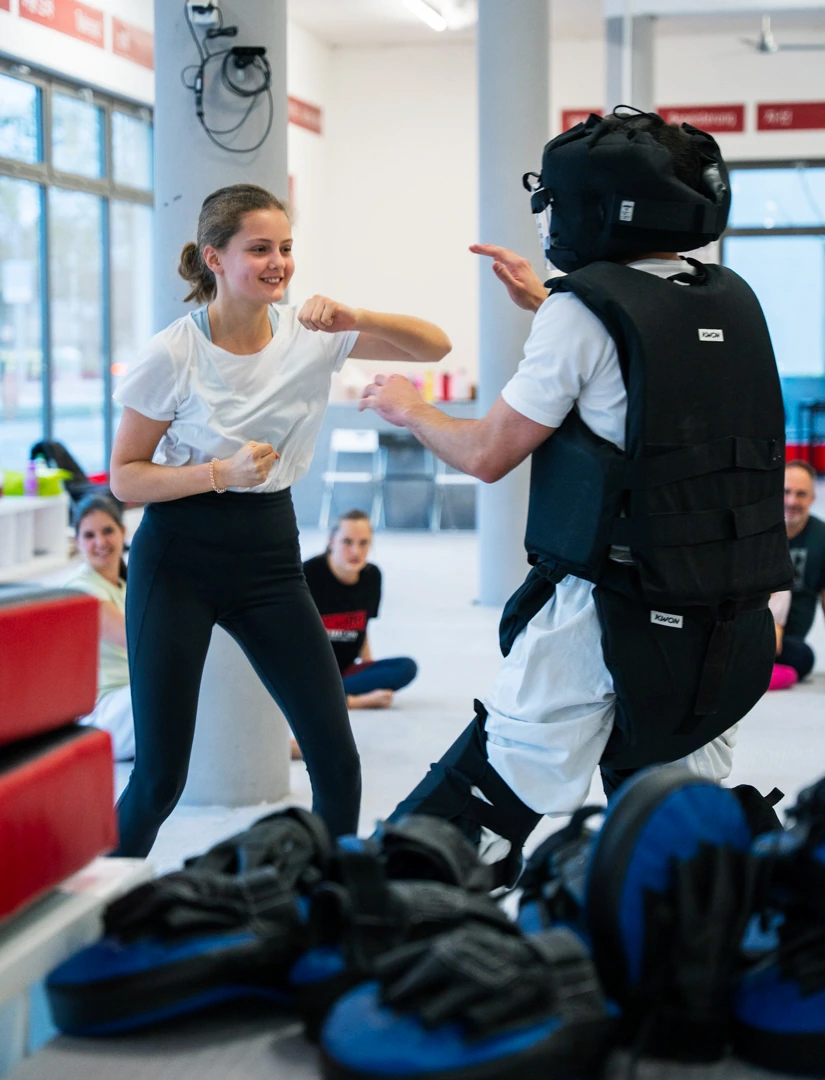 Selbstverteidigungskurs für Mädchen: Schülerin übt Schlag gegen Trainer in Schutzausrüstung.