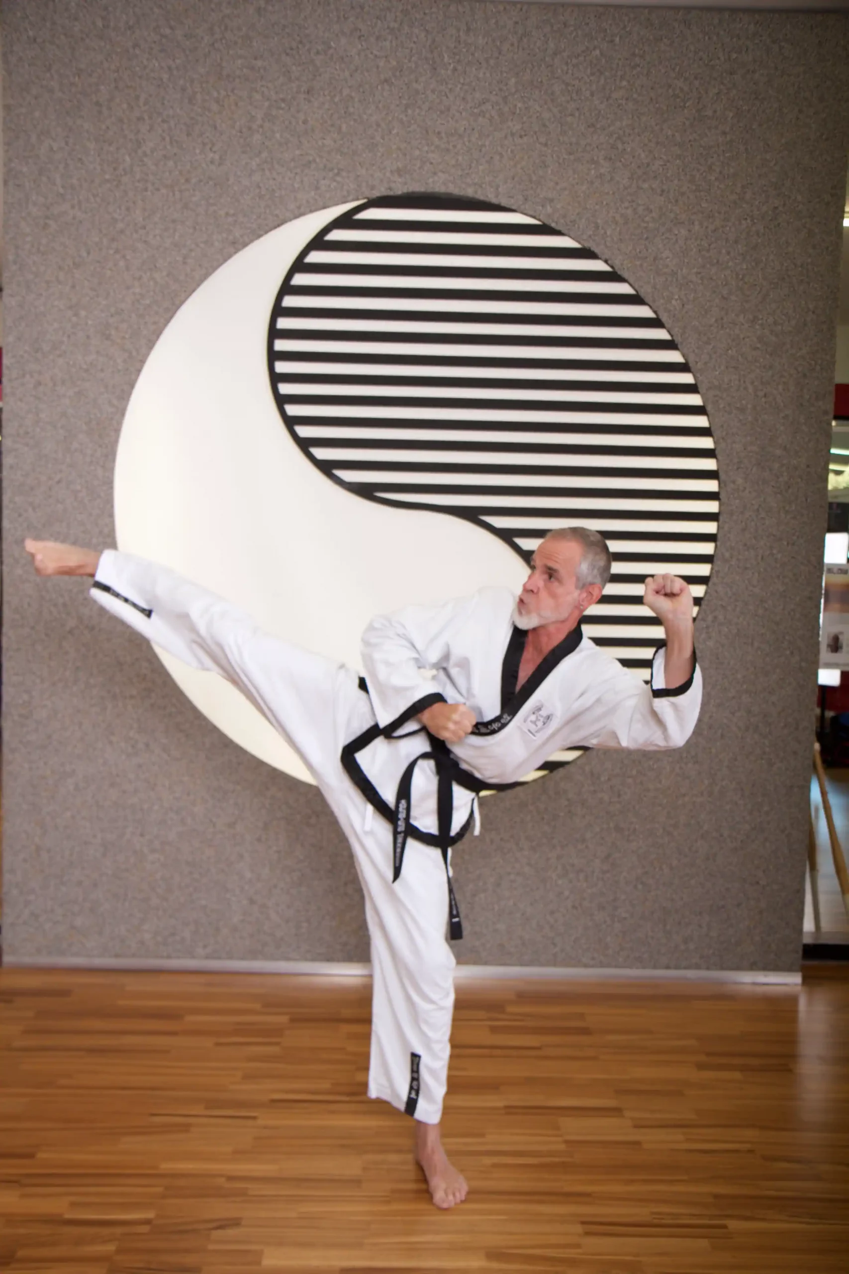 Senior beim Training für traditionelles Taekwondo: Ein Mann mit Schwarzgurt führt einen präzisen hohen Seitwärtstritt aus.