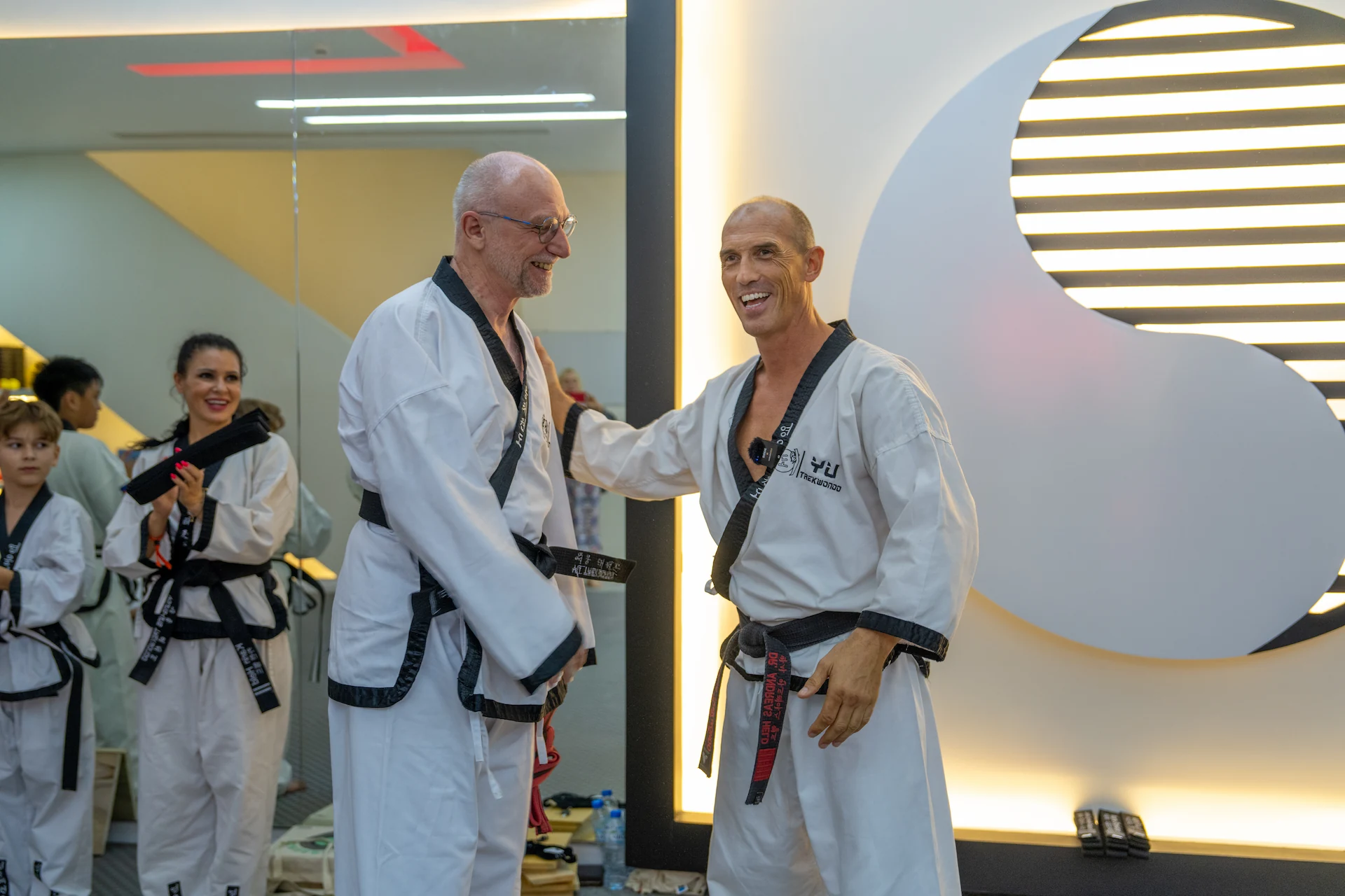 Ein lachender Taekwondo-Trainer im Dobok gratuliert einem Schüler zur bestandenen Prüfung in der Akademie.