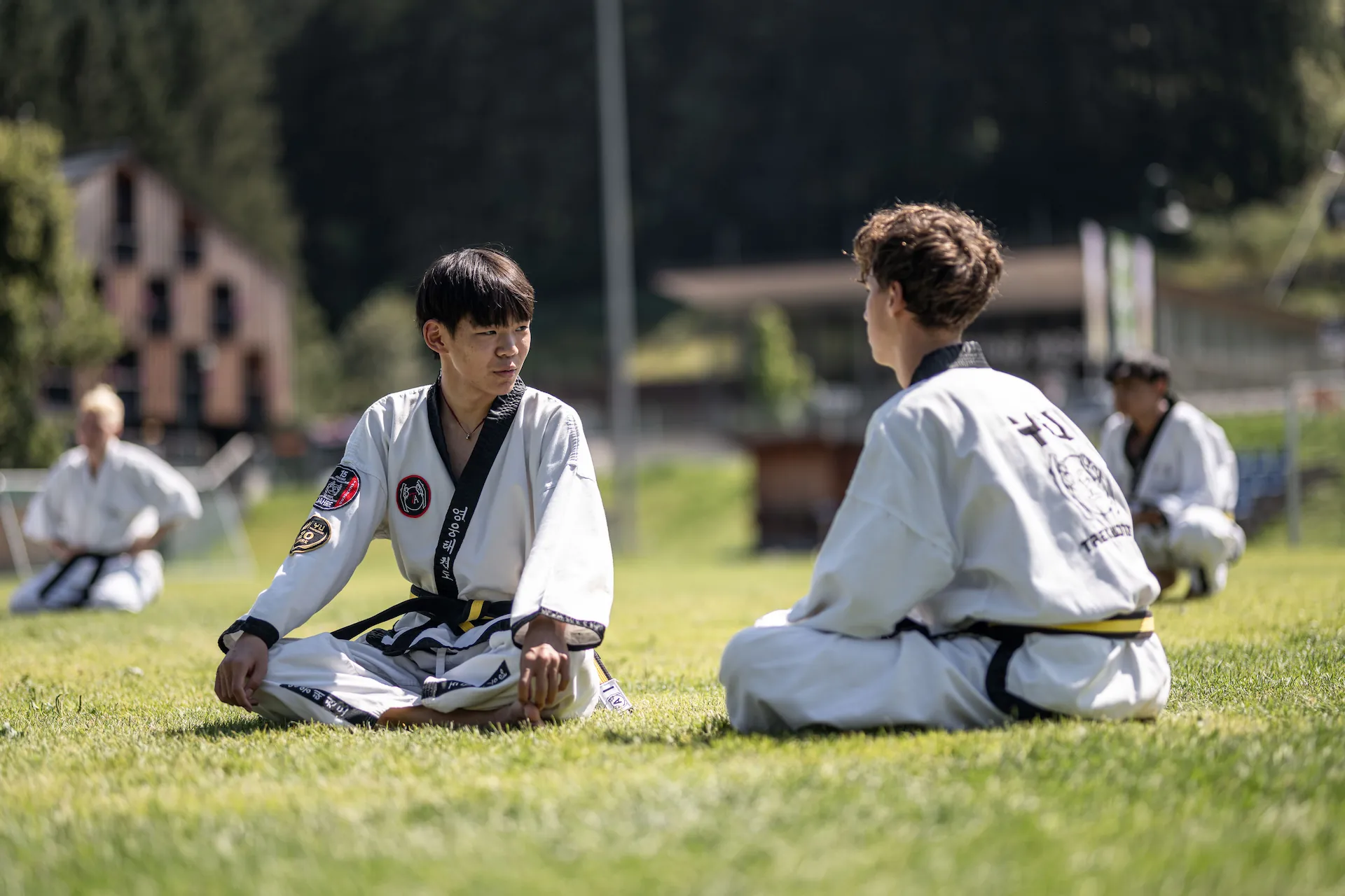 Jugendliche stärken die soziale Gemeinschaft durch Austausch beim Taekwondo-Training im Freien auf einer Wiese.