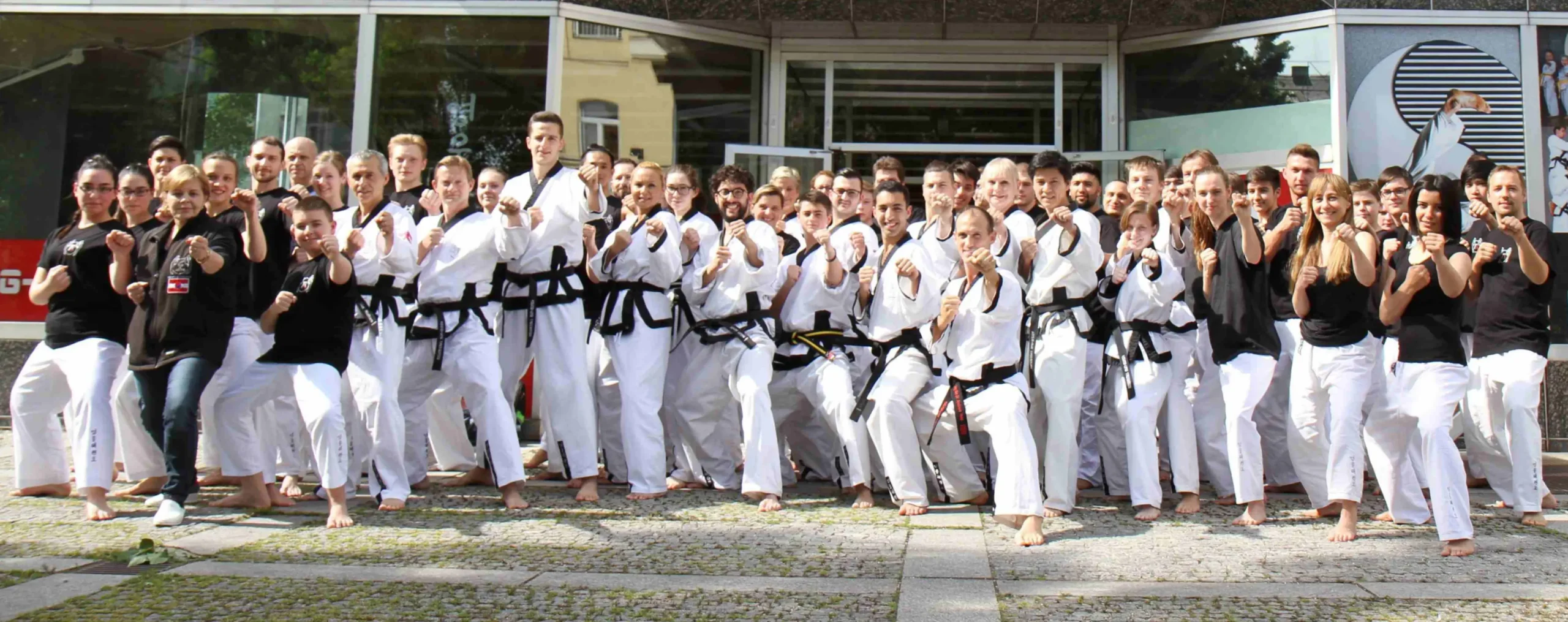 Das Trainer-Team der Akademie posiert in Kampfsport-Anzügen vor dem Eingang der Schule für ein Gruppenfoto.