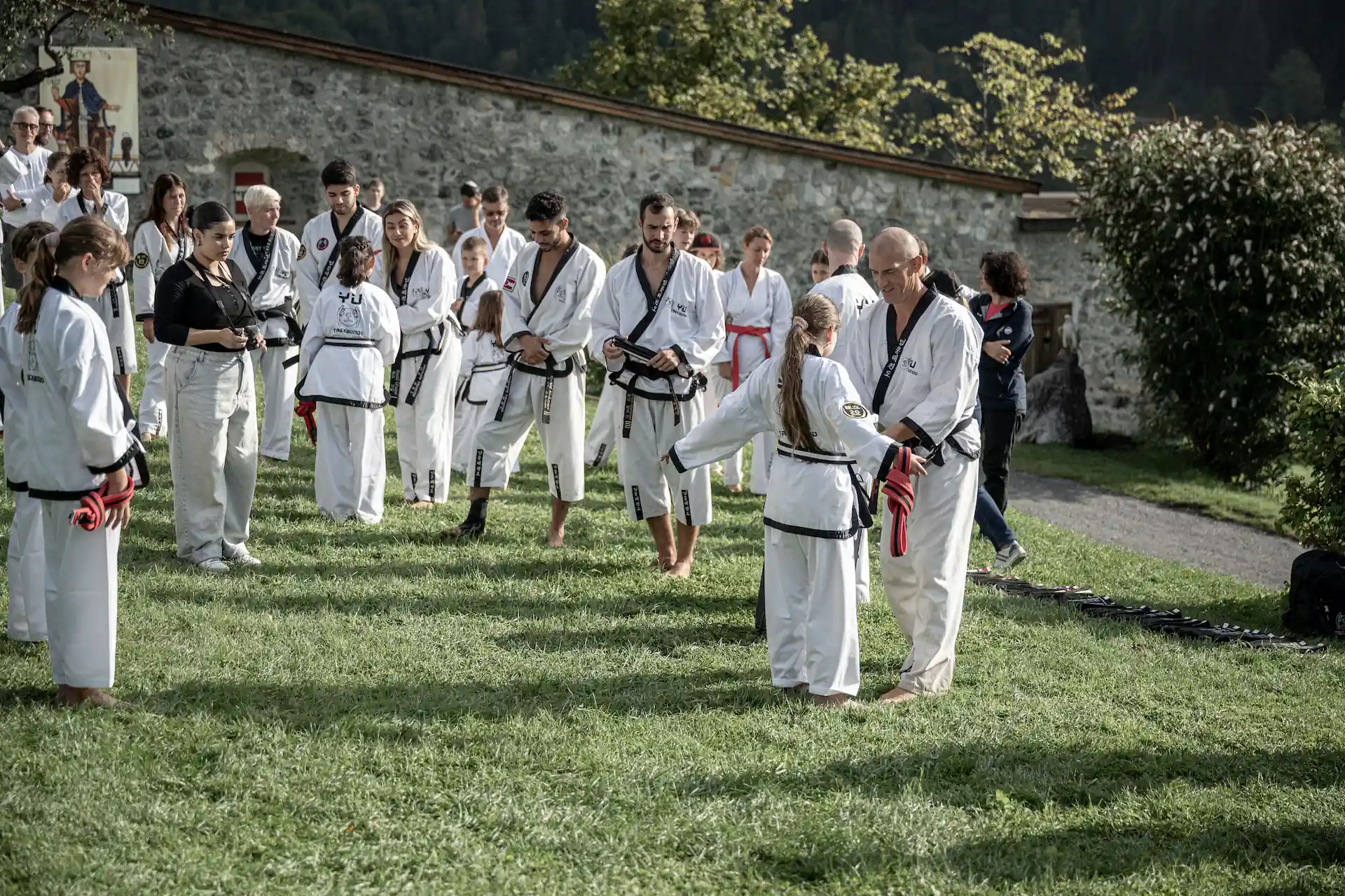 Teilnehmer eines Urlaubs-Camps beim Taekwondo-Training im Freien vor einer historischen Steinmauer.